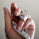 Keine Abnahme trotz Kaloriendefizit symbolisiert durch eine Hand mit einem weißen Maßband
