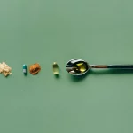 Grüner Hintergrund, darauf Tabletten, Pulver und Kapseln sowie ein Löffel. Die Produkte symbolisieren magnesium citrat.