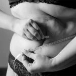 Übergewichtige Frau mit Maßband um den Bauch signalisiert Vitamin B12-Mangel Gewichtszunahme