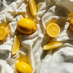 Gelbe Zitronen als Symbol für Vitamin C Pulver liegen auf einer weißen Decke.